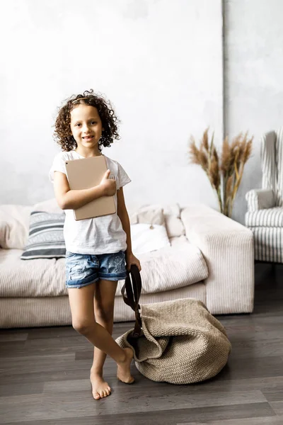 Menina bonito com cabelo encaracolado detém um enorme saco de malha e tablet — Fotografia de Stock