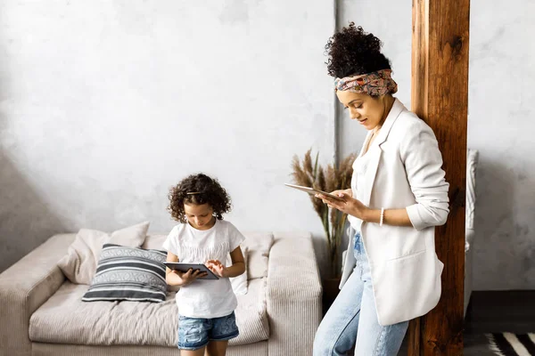 Uma linda mãe e filha conversam e olham para o tablet enquanto estão na sala de estar — Fotografia de Stock