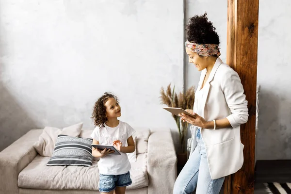 Uma linda mãe e filha conversam e olham para o tablet enquanto estão na sala de estar — Fotografia de Stock