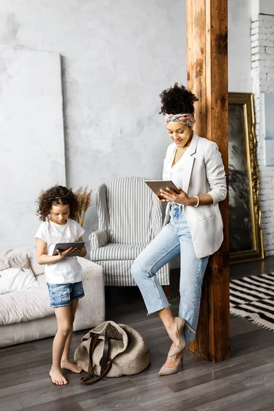 Uma linda mãe e filha conversam e olham para o tablet enquanto estão na sala de estar — Fotografia de Stock