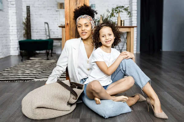 Uma menina encaracolado bonito e sua mãe estão sentados na sala de estar no chão — Fotografia de Stock