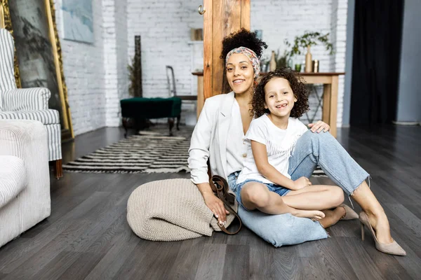 Uma menina encaracolado bonito e sua mãe estão sentados na sala de estar no chão — Fotografia de Stock