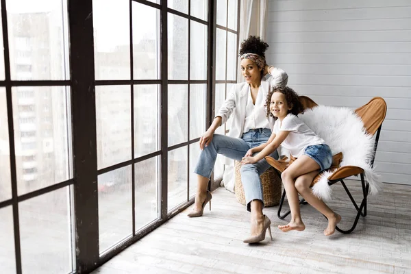 Uma linda mãe e filha sentadas nas poltronas perto da grande janela — Fotografia de Stock