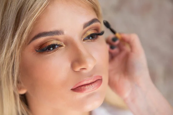 Un maquillador hace un maquillaje para una chica rubia espasmódica —  Fotos de Stock