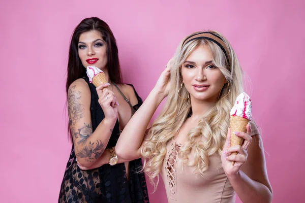 Dos chicas - rubia y morena comiendo helado sobre un fondo rosa — Foto de Stock