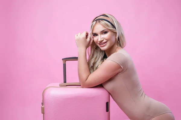Joven chica bonita rubia posando sobre fondo rosa con maleta — Foto de Stock