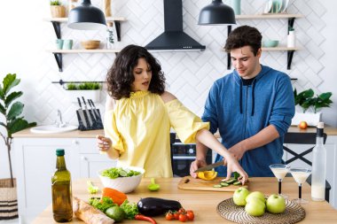 Genç, sevimli, gülümseyen bir çift mutfakta birlikte yemek pişiriyor. Gençler iyi bir mutfakta salata hazırlıyorlar.