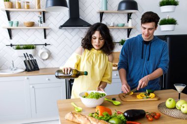 Genç, sevimli, gülümseyen bir çift mutfakta birlikte yemek pişiriyor. Gençler iyi bir mutfakta salata hazırlıyorlar.