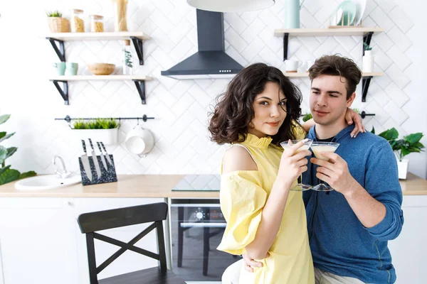 Young cute couple - a boy and a girl romantically spend time in the kitchen. A couple drinks alcohol and prepares a salad. Young cute smiling couple cooking together at kitchen at home