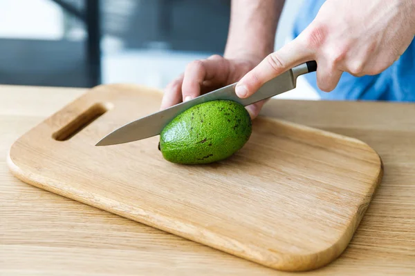 Um rapaz a cortar um abacate numa tábua de madeira para salada. Cozinhar — Fotografia de Stock