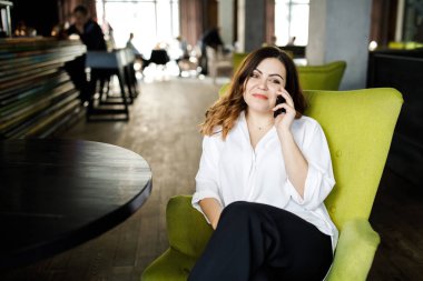 Güzel gülümseyen genç kadın kafede sandalyede oturan elbise giymiş, cep telefonu, şık iç konuşma