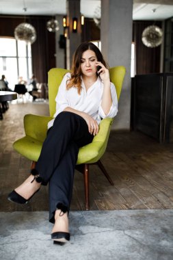 Güzel gülümseyen genç kadın kafede sandalyede oturan elbise giymiş, cep telefonu, şık iç konuşma