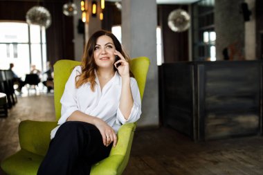 Güzel gülümseyen genç kadın kafede sandalyede oturan elbise giymiş, cep telefonu, şık iç konuşma