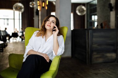 Güzel gülümseyen genç kadın kafede sandalyede oturan elbise giymiş, cep telefonu, şık iç konuşma