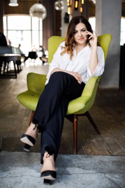 Güzel gülümseyen genç kadın kafede sandalyede oturan elbise giymiş, cep telefonu, şık iç konuşma