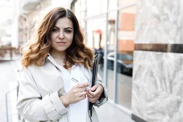 Une jeune femme sympathique, pas une musculation à tête fine, tient un dossier de papier dans ses mains. Joyeux jeune femme d'affaires avec un dossier à l'immeuble de bureaux dans ses mains — Photo