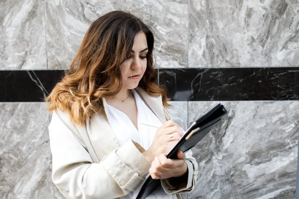 Une jeune femme sympathique, pas une musculation à tête fine, tient un dossier de papier dans ses mains. Joyeux jeune femme d'affaires avec un dossier à l'immeuble de bureaux dans ses mains — Photo