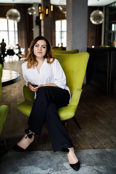 Güzel gülümseyen genç kadın kafede sandalyede oturan elbise giymiş, cep telefonu, şık iç konuşma