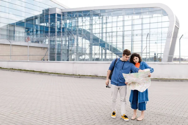 Jovem casal bonito - um menino e uma menina andando pela cidade com um mapa e câmera em suas mãos. Jovens viajam . — Fotografia de Stock