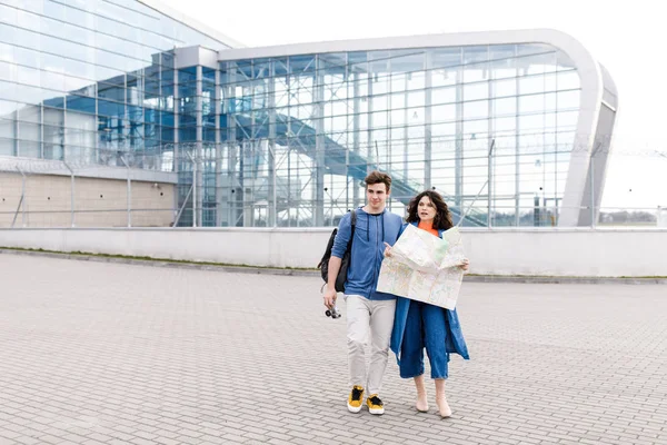 Joven linda pareja - un niño y una niña caminando por la ciudad con un mapa y una cámara en sus manos. Jóvenes viajan . — Foto de Stock