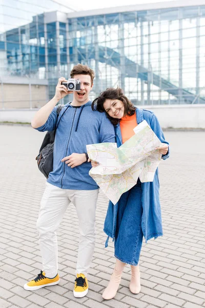 Joven linda pareja - un niño y una niña caminando por la ciudad con un mapa y una cámara en sus manos. Jóvenes viajan . — Foto de Stock