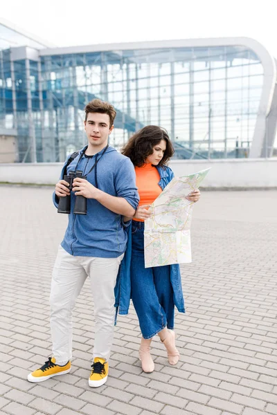 Jovem casal bonito - um menino e uma menina andando pela cidade com um mapa e binóculos em suas mãos. Jovens viajam . — Fotografia de Stock