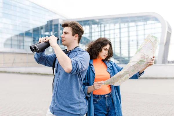 Jovem casal bonito - um menino e uma menina andando pela cidade com um mapa e binóculos em suas mãos. Jovens viajam . — Fotografia de Stock