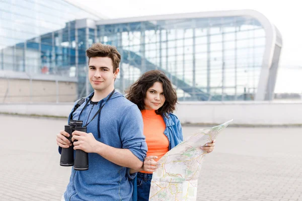 Νεαρό χαριτωμένο ζευγάρι - ένα αγόρι και ένα κορίτσι που περπατούν στην πόλη με ένα χάρτη και κυάλια στα χέρια του. Οι νέοι ταξιδεύουν. — Φωτογραφία Αρχείου