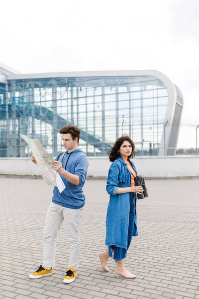 Joven linda pareja - un niño y una niña caminando por la ciudad con un mapa y prismáticos en sus manos. Jóvenes viajan . — Foto de Stock