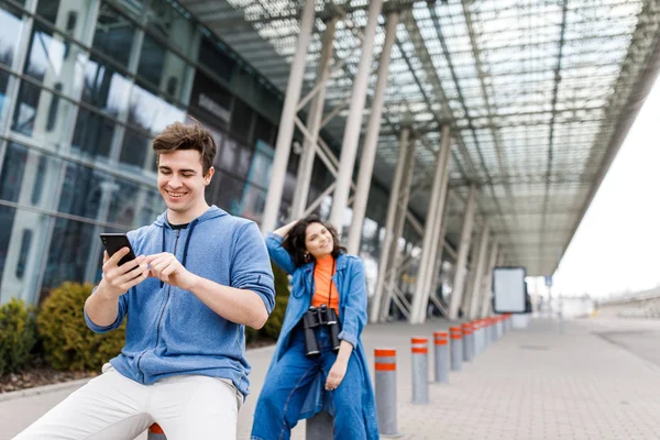 Il tient le téléphone entre ses mains. Jeune couple mignon un garçon et une fille voyagent autour de la ville avec des jumelles dans les mains. Les jeunes voyagent . — Photo