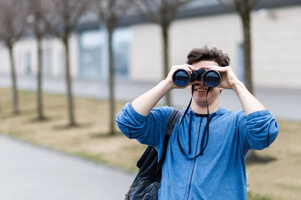 Un chico joven y guapo mantiene los prismáticos en sus brazos y mira a través de él — Foto de Stock