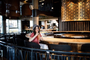 Young pretty cute brunette sitting in a restaurant behind a bar and drinking a cocktail. Summer style