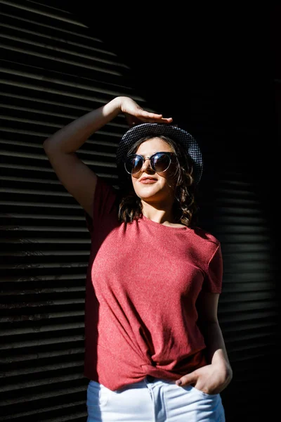 युवा सुंदर श्यामला एक धूप के दिन शहर के चारों ओर घूम रही है, गर्मियों के कपड़े पहने हुए, और उसके सिर पर एक टोपी। ग्रीष्मकालीन शैली — स्टॉक फ़ोटो, इमेज