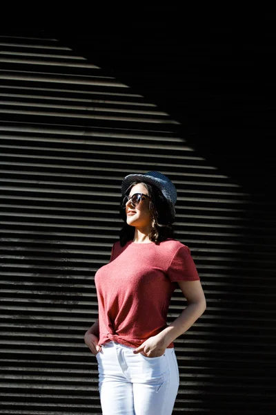 Jeune jolie brune se promenant dans la ville par une journée ensoleillée, vêtue de vêtements d'été, et un chapeau sur la tête. Style d'été — Photo
