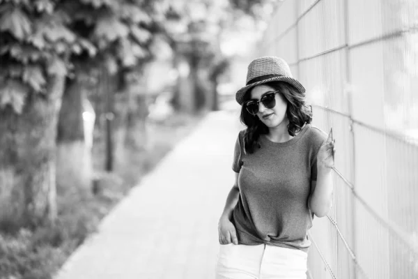 Fiatal, csinos barna nő sétálgat a városban egy napsütéses napon, nyári ruhákba öltözve, és kalap van a fején. Nyári stílus — Stock Fotó