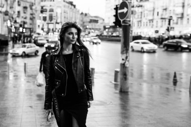 Young pretty girl walking along the street in a dress and a jacket, with a phone in her hands