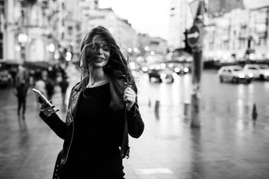 Young pretty girl walking along the street in a dress and a jacket, with a phone in her hands