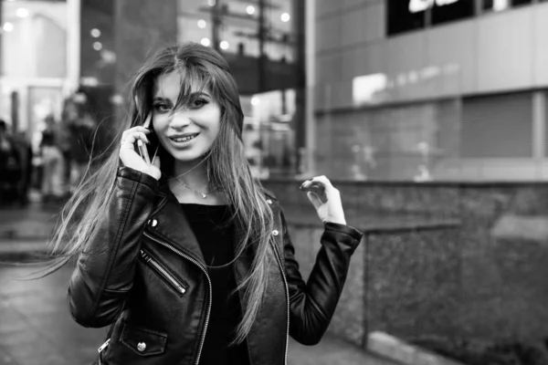 Joven chica bonita caminando por la calle con un vestido y una chaqueta, con un teléfono en las manos — Foto de Stock
