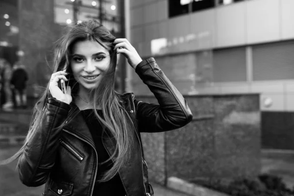 Joven chica bonita caminando por la calle con un vestido y una chaqueta, con un teléfono en las manos — Foto de Stock