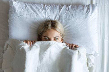 Mutlu sabahlar. Beyaz yatakta rahatlatıcı gülümseyen güzel bir genç sarışın kadının Portresi.