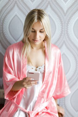 Çekici genç kız evde akıllı telefonu ile bir pijama duruyor. Ev çekimi.