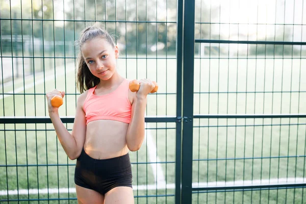 En ung, sympatisk flicka av slank kropp, klädd i en form av idrott, utför utomhus övningar — Stockfoto