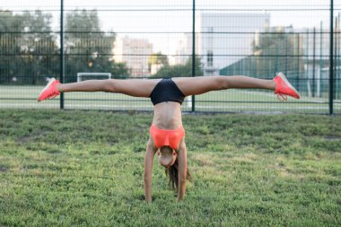 İnce vücut inşa Genç, sempatik kız, spor şeklinde giyinmiş, açık havada jimnastik egzersizleri gerçekleştirir