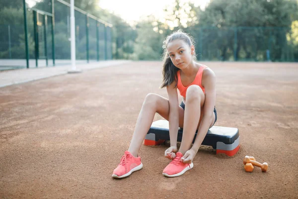 A cute, pretty teenage girl sits on a step platform and relaxes after her workout on outdoor — Stock Photo, Image