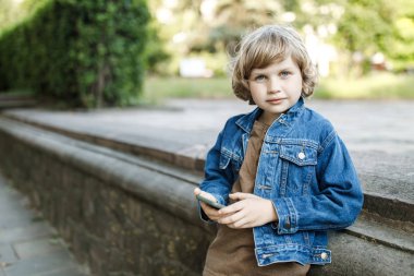 Sevimli sarışın adam, sokakta okul yılı eğlenceli çalışan zaman ve elinde bir akıllı telefon tutar