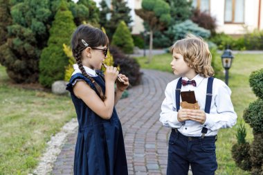 Sevimli sarışın adam ve sevimli kız, okul yılı eğlenceli zaman açık havada. Çocuklar çikolata yer. Okul üniforması giymiş çocuklar parkta oyun oynar