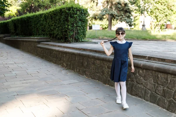 Uma menina bonita estudante está se divertindo na rua no parque. A menina está vestida com uniforme escolar — Fotografia de Stock