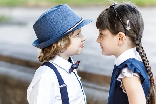 Cute blond guy and cute girl, school year fun time outdoors. Children dressed in school uniform play games in the park