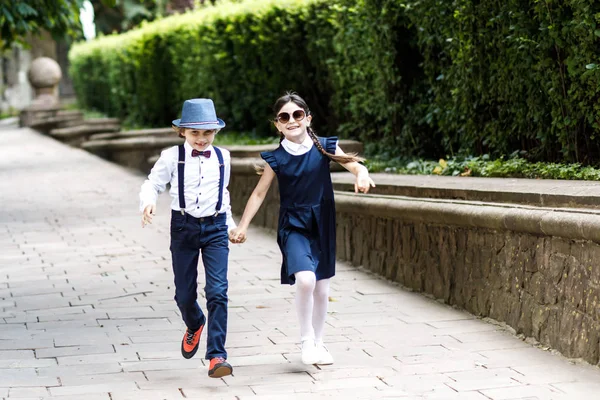 Cara loira bonito e menina bonito, tempo de diversão do ano letivo ao ar livre. Crianças vestidas com uniforme escolar brincam no parque — Fotografia de Stock