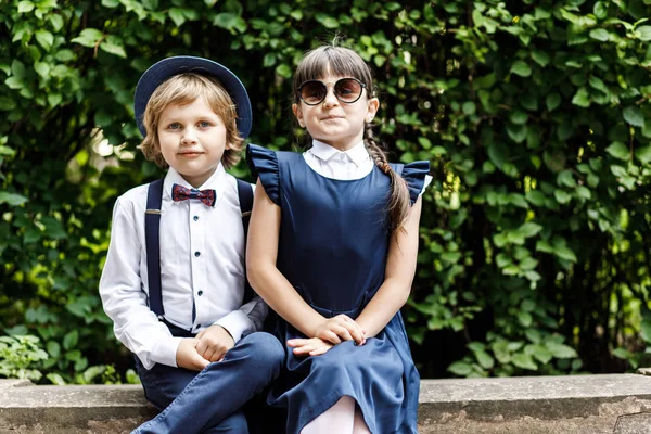 Cute blond guy and cute girl, school year fun time outdoors. Children dressed in school uniform play games in the park